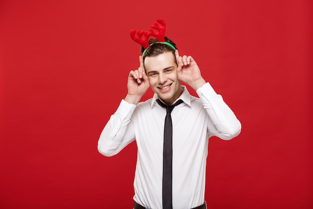 Weihnachtskonzept Gutaussehender Geschäftsmann feiert frohe Weihnachten und ein gutes neues Jahr, trägt Rentierhaarband und hält Hasengeste