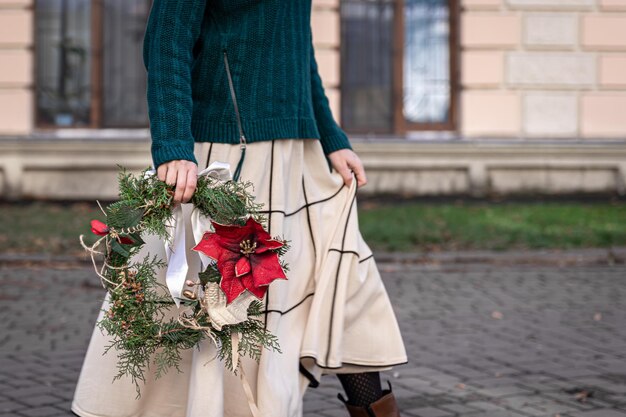 Weihnachtskranz in den Händen eines stilvollen Frauenstadtspaziergangs