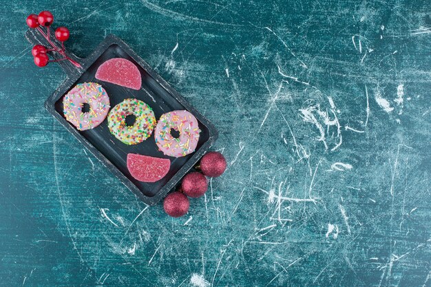 Weihnachtskugeln neben Donuts und Marmeladen auf einer kleinen Platte auf Blau.