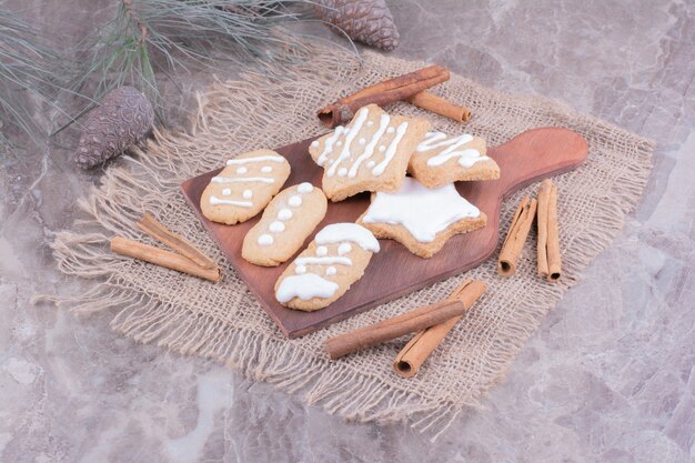 Weihnachtslebkuchen in Oval- und Sternform auf einem Holzbrett mit Zimtstangen herum