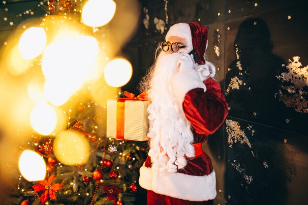 Weihnachtsmann, der am Telefon spricht und ein Geschenk hält