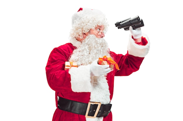 Weihnachtsmann mit einem luxuriösen weißen Bart, der Weihnachtsmannmütze und einem roten Kostüm lokalisiert auf einem weißen Hintergrund mit Fernglas