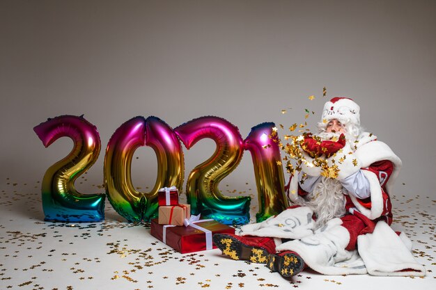 Weihnachtsmann sitzt auf dem Boden mit Geschenken und Luftballons 2021.