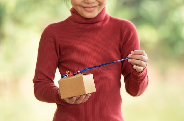 Weihnachtsporträt des glücklichen lächelnden kindes des kleinen mädchens mit geschenkbox nahe einem grünen zweigbaum. grüne blätter bokeh unscharf hintergrund aus dem naturwald.