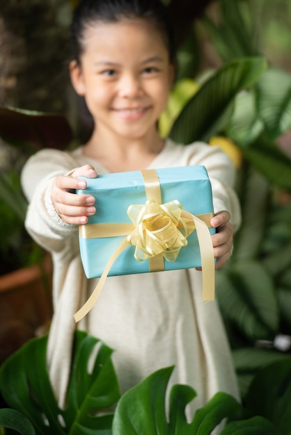 Weihnachtsporträt des glücklichen lächelnden Kindes des kleinen Mädchens mit Geschenkbox nahe einem grünen Zweigbaum.