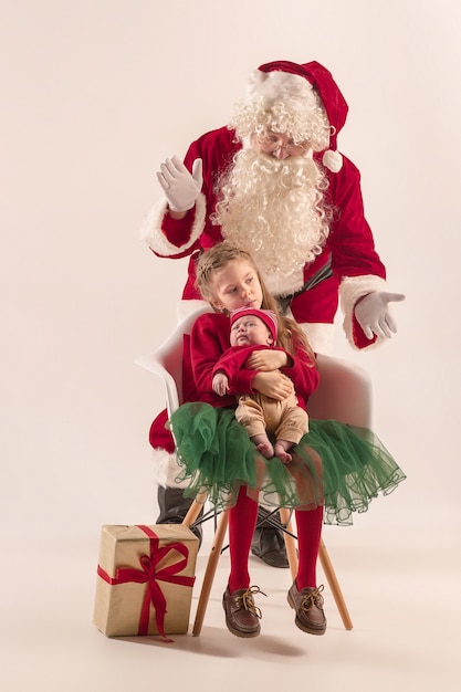 Weihnachtsporträt des niedlichen kleinen Neugeborenen, hübsche jugendlich Schwester, gekleidet in Weihnachtskleidung und Weihnachtsmann mit Geschenkbox