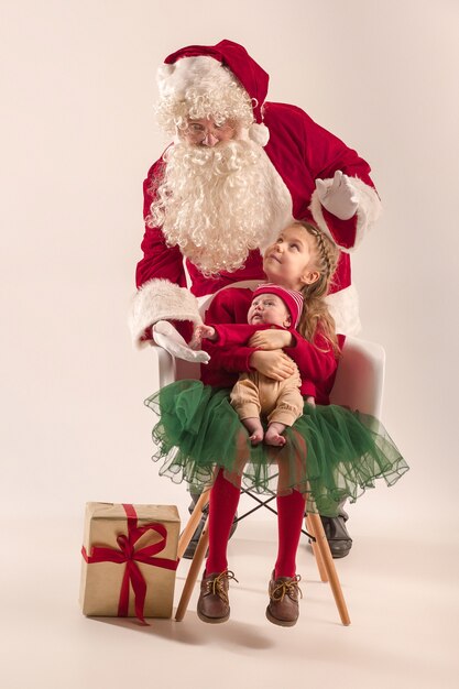 Weihnachtsporträt des niedlichen kleinen Neugeborenen, hübsche jugendlich Schwester, gekleidet in Weihnachtskleidung und Weihnachtsmann mit Geschenkbox