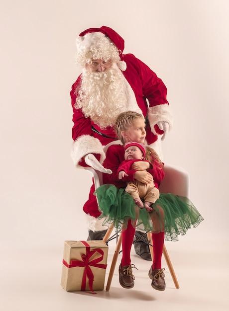 Weihnachtsporträt des niedlichen kleinen neugeborenen Mädchens, der hübschen jugendlich Schwester, gekleidet in Weihnachtskleidung und Mann, der Weihnachtsmannkostüm und -hut, Studioaufnahme, Winterzeit trägt. Das Weihnachts-, Feiertagskonzept