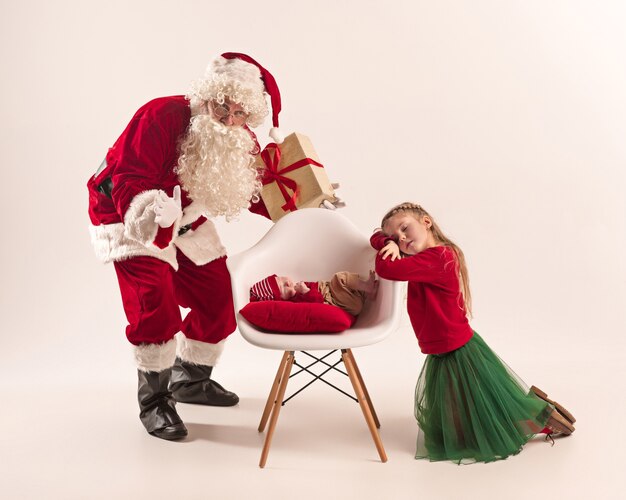 Weihnachtsporträt des niedlichen kleinen neugeborenen Mädchens und der hübschen jugendlich Schwester gekleidet in Weihnachtskleidung und Mann, der Weihnachtsmannkostüm und -hut trägt