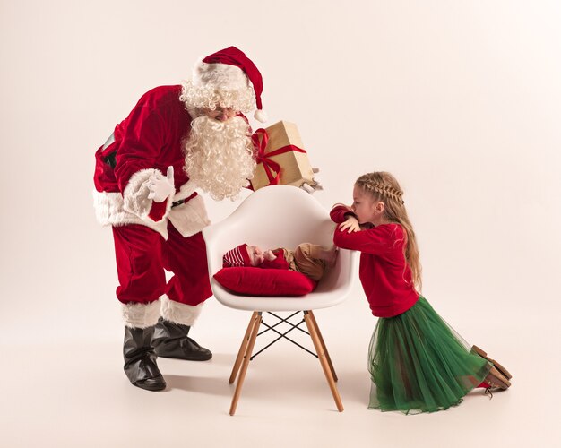 Weihnachtsporträt des niedlichen kleinen neugeborenen Mädchens und der hübschen jugendlich Schwester gekleidet in Weihnachtskleidung und Mann, der Weihnachtsmannkostüm und -hut trägt