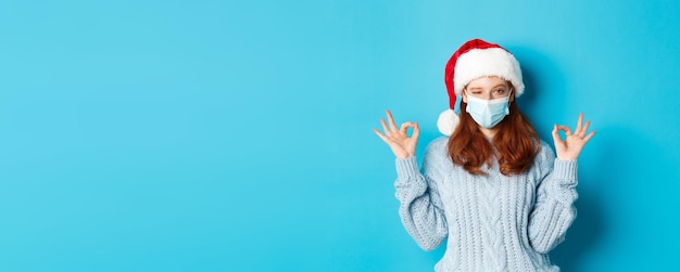 Weihnachtsquarantäne und Covid-Konzept Süßes jugendlich rothaariges Mädchen in Weihnachtsmütze und Pullover mit Gesicht