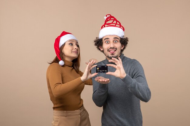 Weihnachtsstimmung mit aufgeregtem zufriedenem coolem Paar, das rote Weihnachtsmannhüte trägt, die Bankkarte zeigen