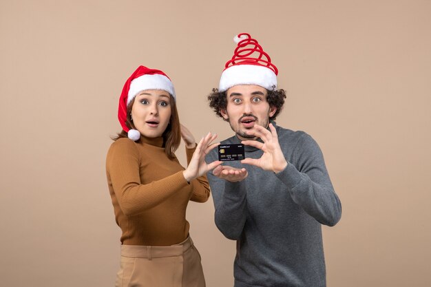 Weihnachtsstimmung mit aufgeregtem zufriedenem coolem Paar, das rote Weihnachtsmannhüte trägt, die glücklich Bankkarte zeigen