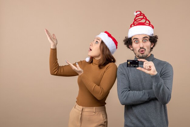 Weihnachtsstimmung mit aufgeregtem zufriedenem schockiertem coolem Paar, das rote Weihnachtsmannhüte trägt, die Bankkarte zeigen