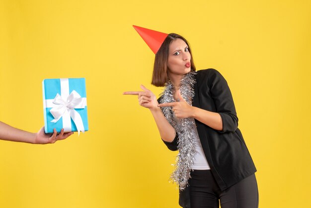 Weihnachtsstimmung mit aufgeregter Geschäftsdame im Anzug mit Weihnachtshut, der die Hand zeigt, die Geschenk auf Gelb hält