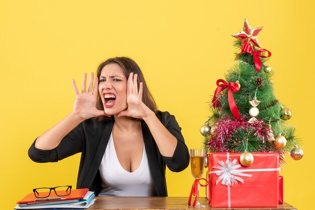 Weihnachtsstimmung mit der jungen angespannten Geschäftsdame, die jemanden anruft und im Büro auf Gelb sitzt