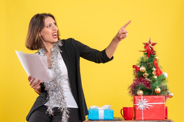 Weihnachtsstimmung mit emotionaler nervöser schöner Dame, die im Büro steht und Dokumente im Büro auf Gelb hält