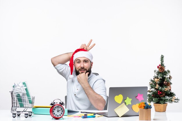 Weihnachtsstimmung mit jungem Erwachsenen mit seinem Weihnachtsmann, der zwei hinter seinem Kopf zeigt und im Büro an einem Projekt beteiligt ist