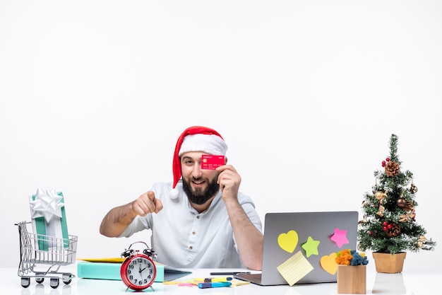 Weihnachtsstimmung mit jungem Erwachsenen mit Weihnachtsmann-Hut und Bankkarte zeigen und etwas im Büro zeigen