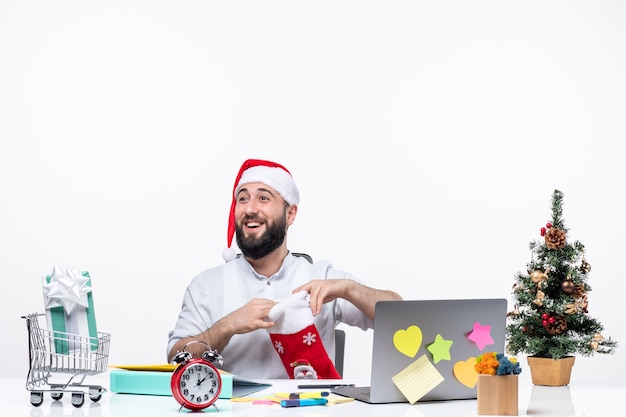 Weihnachtsstimmung mit jungem erwachsenen mit weihnachtsmann-hut und öffnen seiner weihnachtssocke mit blick auf jemanden im büro