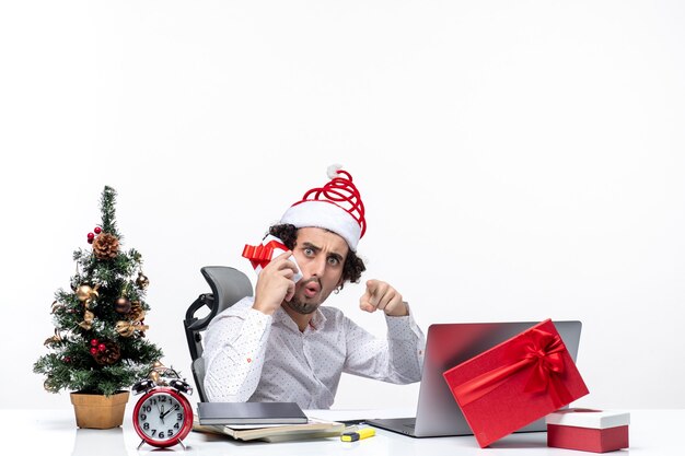 Weihnachtsstimmung mit jungen bärtigen schockierten Geschäftsmann mit Weihnachtsmannhut, der sein Geschenk erhöht und etwas auf dunklem Hintergrund zeigt