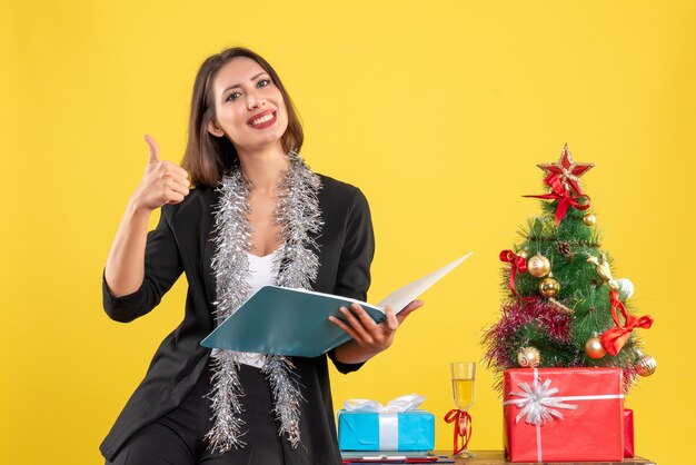 Weihnachtsstimmung mit lächelnder schöner Dame, die im Büro steht und alleine arbeitet und ok Geste im Büro macht