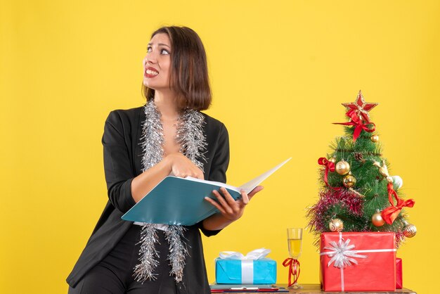 Weihnachtsstimmung mit neugieriger schöner Dame, die im Büro steht und allein im Büro auf Gelb arbeitet