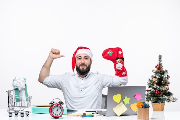 Weihnachtsstimmung mit positivem jungen erwachsenen mit weihnachtsmann-hut und weihnachtssocke an seiner hand, die im büro kraftgeste macht