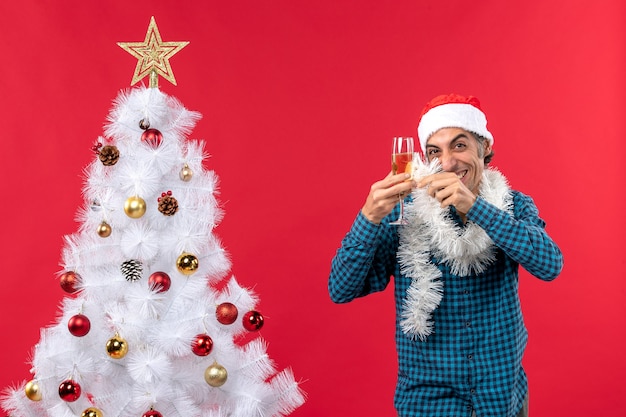 Weihnachtsstimmung mit verrücktem jungem Mann mit Weihnachtsmannhut und einem Glas Wein jubelt sich nahe Weihnachtsbaum