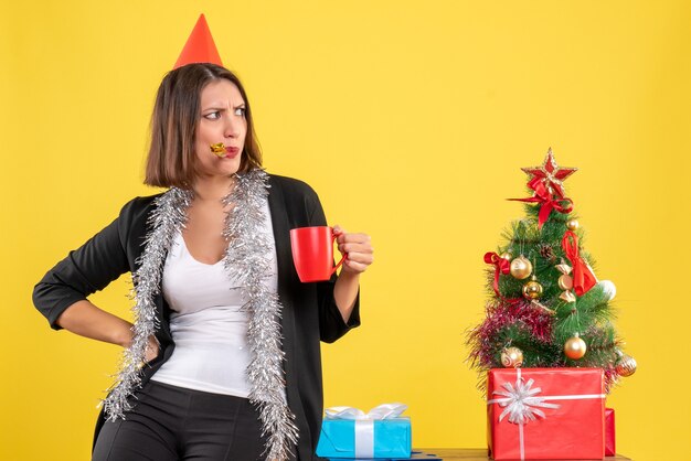 Weihnachtsstimmung mit verwirrter schöner Dame, die die rote Tasse im Büro auf Gelb hält
