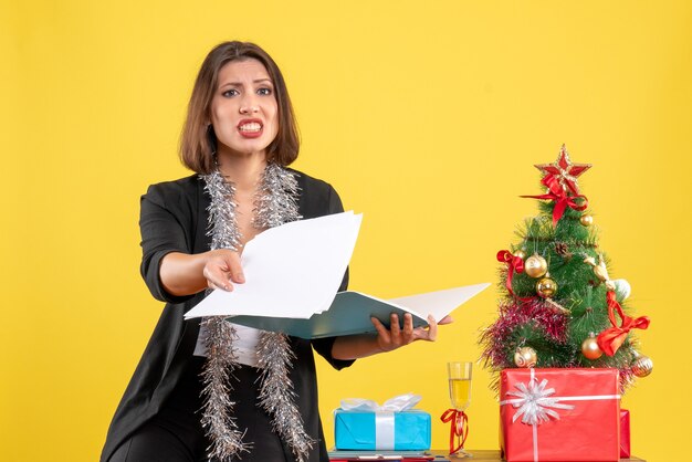 Weihnachtsstimmung mit verwirrter schöner Dame, die im Büro steht und allein im Büro auf Gelb arbeitet