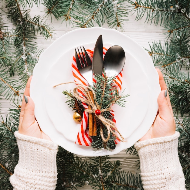 Weihnachtszusammensetzung mit den Händen, die Platte mit Tischbesteck halten