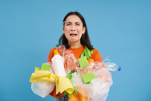 Kostenloses Foto weinende asiatische frau, die plastikmüll in den händen hält und verärgert aussieht, muss blauen bac recyceln