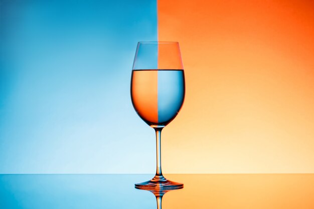 Weinglas mit Wasser über blauem und orange Hintergrund.