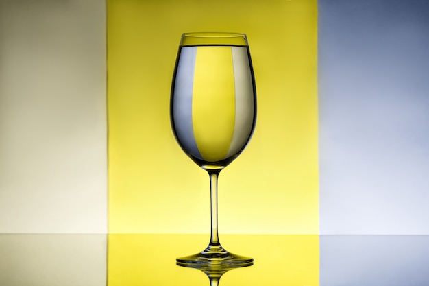 Weinglas mit Wasser über grauem und gelbem Hintergrund.