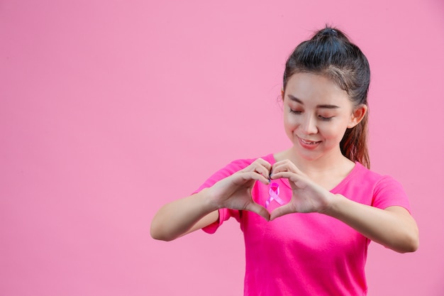 Weiße asiatische Frau, die ein rosa Hemd trägt Handgemachte Herzform auf einem Rosa.