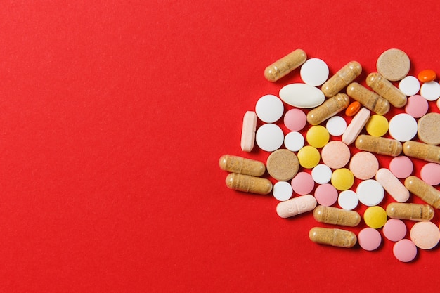 Weiße bunte runde tabletten der medikation arrangierten abstrakt auf rotem farbhintergrund. aspirin, kapselpillen für design. gesundheit, behandlung, gesundes lebensstilkonzept der wahl. platzwerbung kopieren.