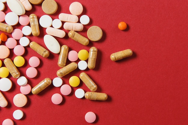 Weiße bunte runde tabletten der medikation arrangierten abstrakt auf rotem farbhintergrund. aspirin, kapselpillen für design. gesundheit, behandlung, gesundes lebensstilkonzept der wahl. platzwerbung kopieren.