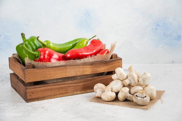 Weiße Champignons mit roten und grünen Chilischoten in einem Holztablett.