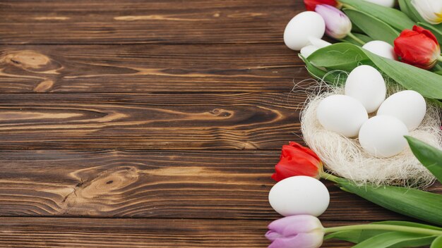 Weiße Eier im Nest mit Tulpen auf Holztisch