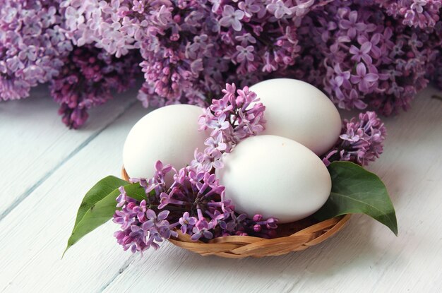 Weiße Eier innerhalb eines lila Korbes und eines Blumenstraußes herum.