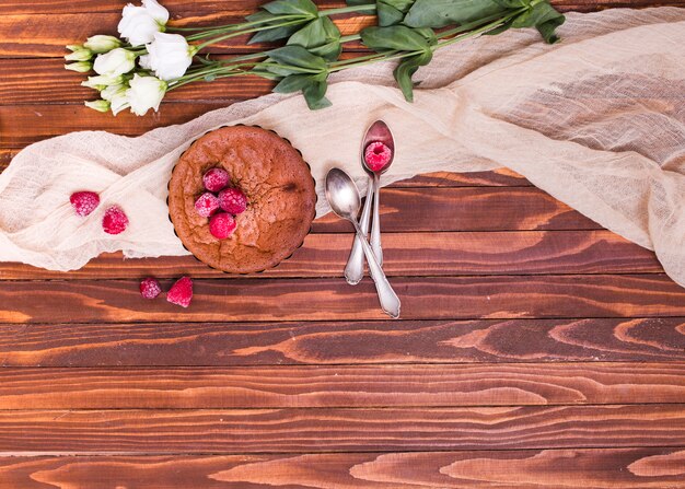 Weiße Eustoma-Blüten; gebacken mit Himbeer-Toppings und Löffel auf Tuch über der Holzoberfläche gebacken