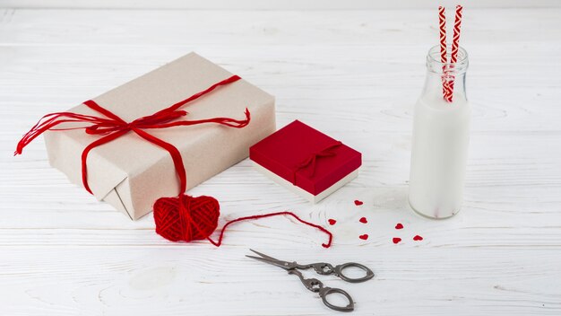 Weiße Flüssigkeit in Flasche mit Tuben in der Nähe von kleinen Herzen, Schere und Geschenken