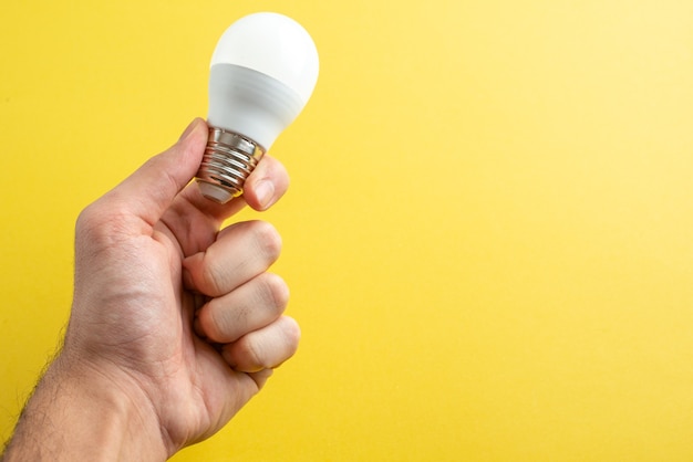Weiße Glühbirne der Vorderansicht auf männlichen Händen auf gelbem Hintergrundfarblichtfoto Elektrizitätshauszimmermensch