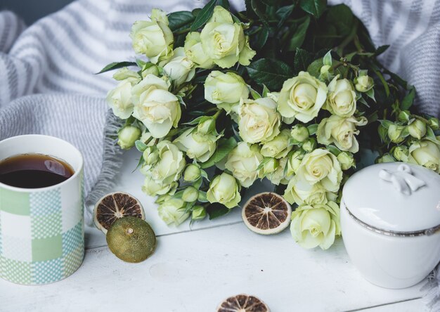 Weiße grüne Rosen und eine Tasse heißen Tee