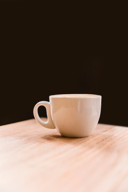 Weiße Kaffeetasse auf Schreibtisch über schwarzem Hintergrund