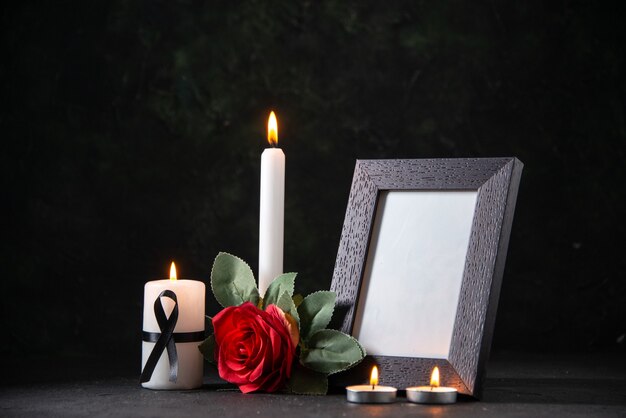 Weiße Kerze der Vorderansicht mit Bilderrahmen und Blume auf dunklem Tod der Beerdigung des dunklen Schreibtisches