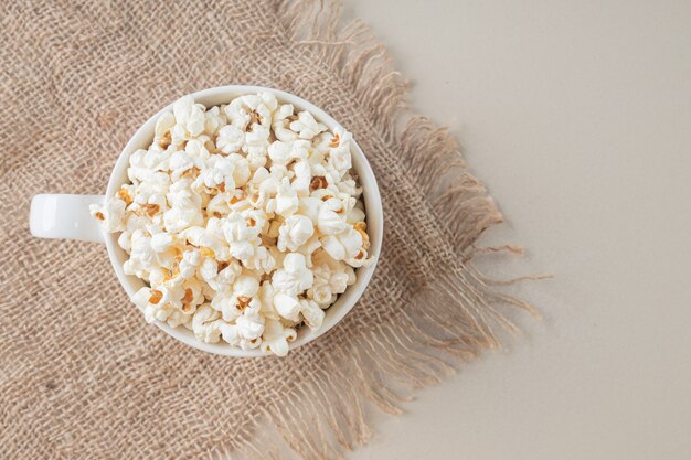 Weiße klassische Popcorns in einer weißen Tasse auf einem Stück Sackleinen.