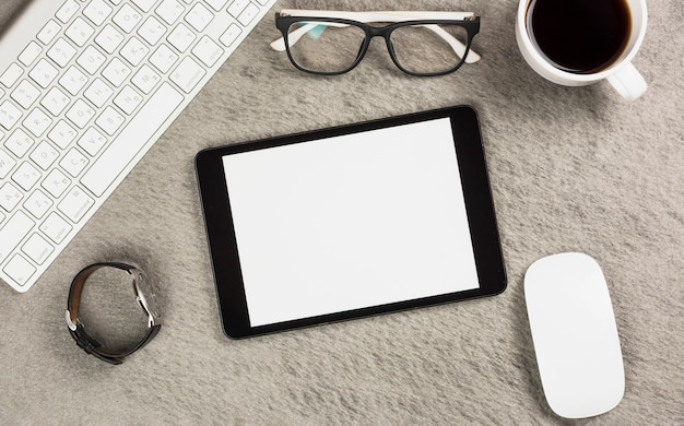 Weiße leere digitale Tablette mit Kaffeetasse; Schauspiel; Maus; Tastatur und Armbanduhr auf grauem Schreibtisch