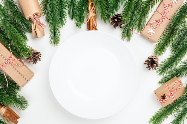 Weiße leere keramikplatte mit kopienraum auf weißem tisch mit weihnachtsdekorationen aus tannenkleie...